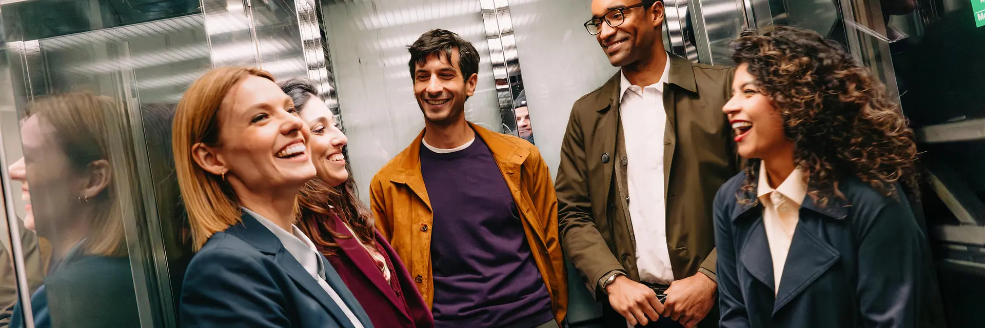 Three women and two men are chatting and laughing in the elevator at an underground station