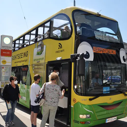 Personen beim Einsteigen in einen gelben Hop-On Hop-Off-Doppeldeckerbus von Vienna Sightseeing
