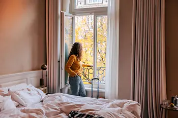 Persona de pie junto a una ventana abierta en la habitación del hotel