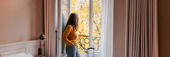 Person steht an geöffnetem Fenster im Hotelzimmer