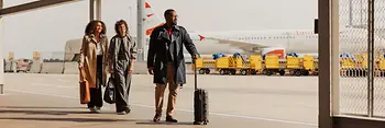 People with carry-on luggage in the outdoor area of Vienna International Airport on their way to the terminal.